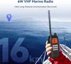 A hand holding a marine radio with the ocean and a boat in the background. Náhled obrázku produktu