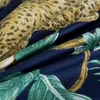 A close-up view of a fabric with a leopard print and tropical leaf pattern on a navy blue background. Náhľad obrázku produktu