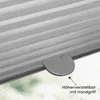 A close-up of a gray pleated blind with a handle, showing a detail of its height adjustment feature. The background shows a blurred outdoor scene. Produktbild-Vorschau