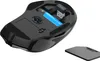 The underside of a black wireless mouse, showing the battery compartment with a blue battery inserted and a USB receiver plugged in. The battery cover is placed next to the mouse. Produktbild-Vorschau