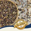 A wooden bowl filled with chopped carob pods, scattered on a wooden surface, with a marketing badge overlay. Produktbild-Vorschau