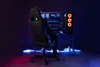A person is sitting in a gaming chair in front of a computer setup, with neon lighting. Produktbild-Vorschau