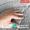 A hand is shown pressing into a soft, textured gray rug. Anteprima dell’immagine prodotto