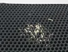 Close-up view of a black honeycomb-patterned litter mat with small beige pellets scattered on it. Náhled obrázku produktu