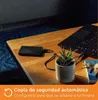 A black external hard drive is connected to a laptop on a wooden desk, with a small potted plant and keys nearby. Voir les images du produit
