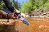 A person is using a water filter straw in a stream. Podgląd zdjęcia produktu