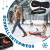A man pulls a woman on a sled through a snowy forest, with deer in the background. A close-up of a tow rope with a handle is in the upper right corner. The trunk of a car with sleds is in the lower left. Produktbild-Vorschau