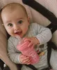 A baby is holding a pink baby bottle. Podgląd zdjęcia produktu