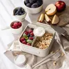 A lunchbox filled with berries, yogurt, and granola, surrounded by fresh fruits and cutlery, set on a neutral fabric surface. Podgląd zdjęcia produktu