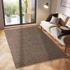 A brown rug is placed on a wooden floor in front of a sofa and a large window. Náhled obrázku produktu