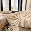 A cozy bedroom scene with a thick, beige blanket draped over a bed, next to a window with sheer curtains. Anteprima dell’immagine prodotto