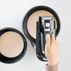 A hand is pressing a button on a black hand mixer that is positioned over a bowl of light-colored batter. Another bowl of batter is visible to the left. Produktbild-Vorschau