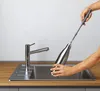 A person is cleaning a metal bottle with a brush in a kitchen sink. Produktbild-Vorschau