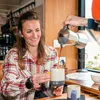 Frau mit langen Haaren; die lächelt und Kaffee aus einer Kaffeekanne in die Climbing Mug Evo Keramiktasse von YY Vertical gießt. Podgląd zdjęcia produktu