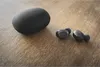 A pair of black wireless earbuds and their charging case are placed on a wooden surface. Anteprima dell’immagine prodotto