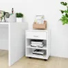 A white rolling cabinet with a drawer and shelves, placed next to a desk, with books and office supplies on top. Podgląd zdjęcia produktu