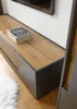 A close-up view of a modern TV stand with a wooden top and dark gray drawers, with a stack of books on top. Produktbild-Vorschau