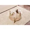 A round coffee table with a glass top and wooden base, decorated with a book, a candle in a tray, and a sculpture, placed on a fluffy rug. Produktbild-Vorschau