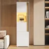 A tall, narrow cabinet with a white front and a natural wood accent, illuminated by warm LED lighting. It is placed in a room with wood-paneled walls and a sofa visible on the left. Anteprima dell’immagine prodotto