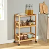 A wooden serving cart with three shelves filled with kitchen items like plates, jars, and bowls, placed against a gray wall. Voir les images du produit