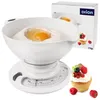 A white kitchen scale with a bowl containing flour and an egg, next to a cupcake and some berries, with the product's packaging in the background. Produktbild-Vorschau