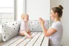 A mother and baby are sitting on a window seat, with the mother clapping her hands and the baby looking at her. Produktbild-Vorschau