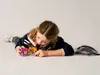 A young girl is lying on the floor playing with small toy cubes. Náhled obrázku produktu