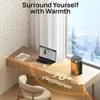 A small electric heater is placed on a desk next to a laptop, with a window showing a snowy landscape in the background. The heater is shown oscillating to distribute warmth. Produktbild-Vorschau