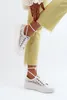 A person's legs and feet wearing white lace sneakers and yellow jeans. Voir les images du produit