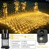 A net of fairy lights draped over decorative figures in a garden setting, with a power adapter and control box shown. Produktbild-Vorschau