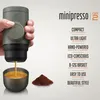 A hand holding a portable espresso maker with coffee brewing into a cup, next to a pile of coffee grounds. Produktbild-Vorschau