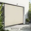 An outdoor scene showing a large beige awning or screen deployed against a white wall, with plants in pots nearby. Náhled obrázku produktu