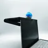 A black monitor stand is placed on top of a laptop, with a small blue and orange decorative item on the stand. Produktbild-Vorschau