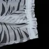 A close-up view of a white sheer curtain with a black leaf pattern and a ruffled edge. Produktbild-Vorschau