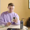 A man is sitting at a table, charging his phone and tablet with a power bank. Produktbild-Vorschau