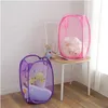 Two pop-up laundry baskets, one purple and one pink, are shown in a room with a chair and a teddy bear. Produktbild-Vorschau