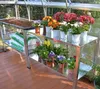 A greenhouse with a metal plant stand holding bags of soil and potted flowers. Náhľad obrázku produktu