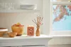 A lit candle sits on a white shelf next to a vase with branches and a bowl of apples. Náhled obrázku produktu
