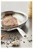 A steak is being seared in a stainless steel frying pan on a speckled countertop, with peppercorns and garlic scattered around. Náhled obrázku produktu