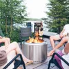People gathered around a fire pit on a wooden deck by a lake. Produktbild-Vorschau