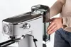 A person's hands are shown interacting with a white espresso machine, specifically near the water tank. Podgląd zdjęcia produktu