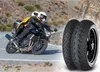 Two people riding a motorcycle on a winding road, with motorcycle tires in the foreground. Produktbild-Vorschau