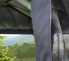 A close-up view of a gray polyester mosquito net with a zipper, attached to a gazebo structure, with a blurred background of trees and mountains. Voir les images du produit