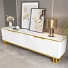 A white TV cabinet with gold accents is shown in a modern living room setting, decorated with artwork and a lamp. Náhľad obrázku produktu