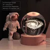 An astronaut figurine stands next to a glowing crystal ball displaying a galaxy, both on a wooden base. Produktbild-Vorschau