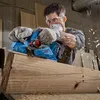 A man is using a blue Bosch power planer on a large piece of wood, creating wood shavings. Podgląd zdjęcia produktu