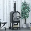 An outdoor pizza oven is shown in a backyard setting, with a white wooden fence in the background and a potted plant to the right. Produktbild-Vorschau