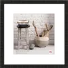 A framed picture of a stool with a basket on top and a pot with branches next to it, set against a brick wall. Náhled obrázku produktu