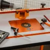A close-up view of a router table with various accessories, including a dust collection attachment and a router template guide set. Produktbild-Vorschau