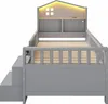 A grey twin-sized bed frame with a house-shaped headboard featuring LED lights and a window cutout. It includes a slatted mattress support, a safety rail, and a staircase with drawers on the side. Anteprima dell’immagine prodotto